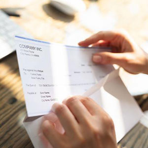 A person holding a check in front of a laptop- Moss Bollinger LLP