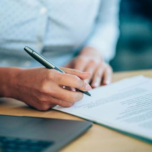 A woman focusedly writes on paper using a pen- Moss Bollinger LLP