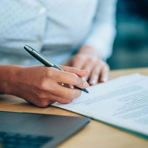 A woman focusedly writes on paper using a pen- Moss Bollinger LLP