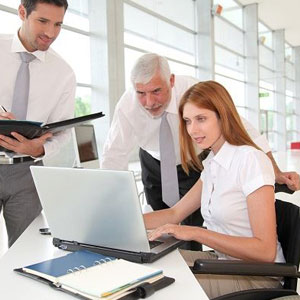 Three professionals in suits examining a laptop screen, engaged in a business discussion- Moss Bollinger LLP