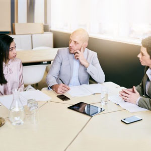 A group of professionals discussing while seated around a table in an office setting- Moss Bollinger LLP