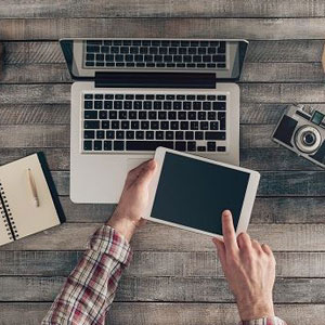 A man using a tablet on a wooden desk, engaged in digital activities- Moss Bollinger LLP