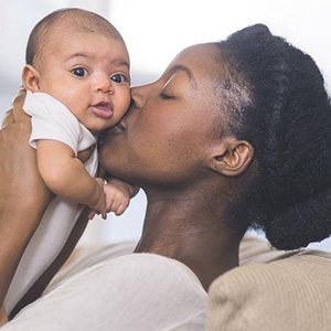 A mother affectionately kisses her baby on a couch, showcasing the bond between them- Moss Bollinger LLP