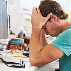 A man sitting at his desk, looking overwhelmed as he rests his head in his hands, deep in thought- Moss Bollinger LLP