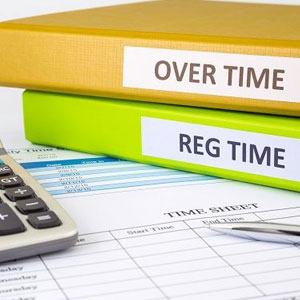 Over Time & Reg Time labeled folders, a calculator, and a timesheet form on a desk- Moss Bollinger LLP