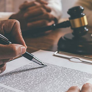 Hand hovers over legal document on wooden desk, gavel in background. Second person clasps hands- Moss Bollinger LLP