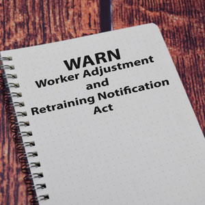 Open notebook with 'WARN' acronym on cover, symbolizing Worker Adjustment and Retraining Notification Act, rests on a contemplative wooden surface- Moss Bollinger LLP