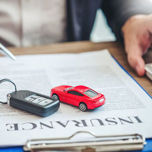 A red toy car and car keys on an insurance document- Moss Bollinger LLP