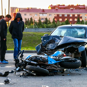 People gathered around damaged motorcycle & car  on a road - Moss Bollinger LLP